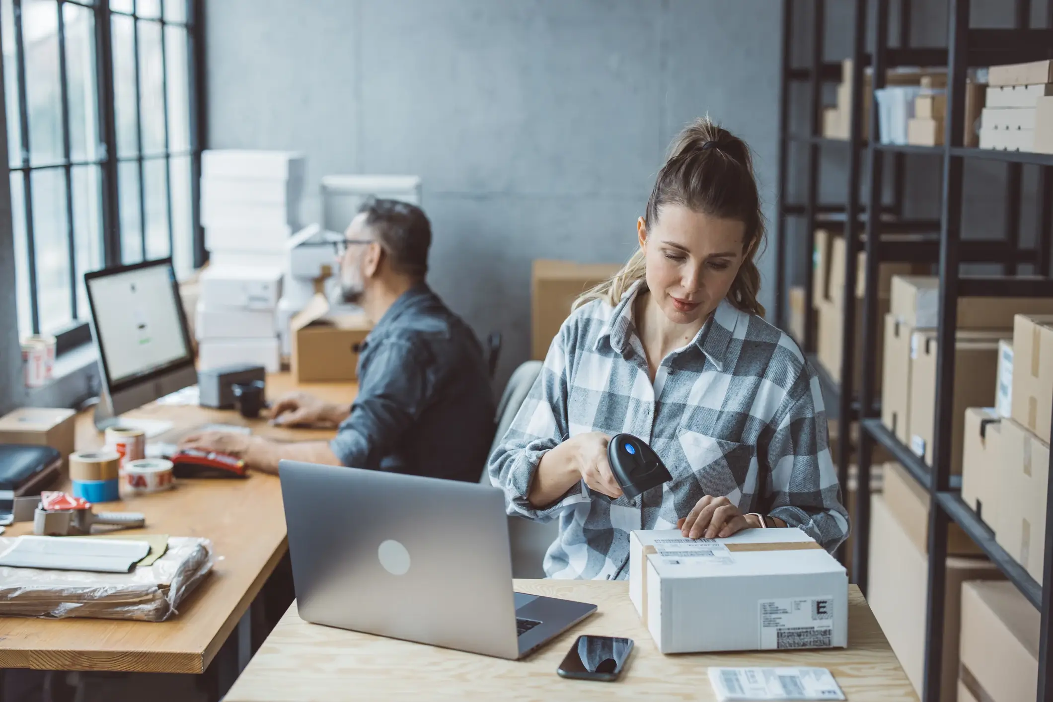 male and female working in a warehouse scanning packages and working on laptops